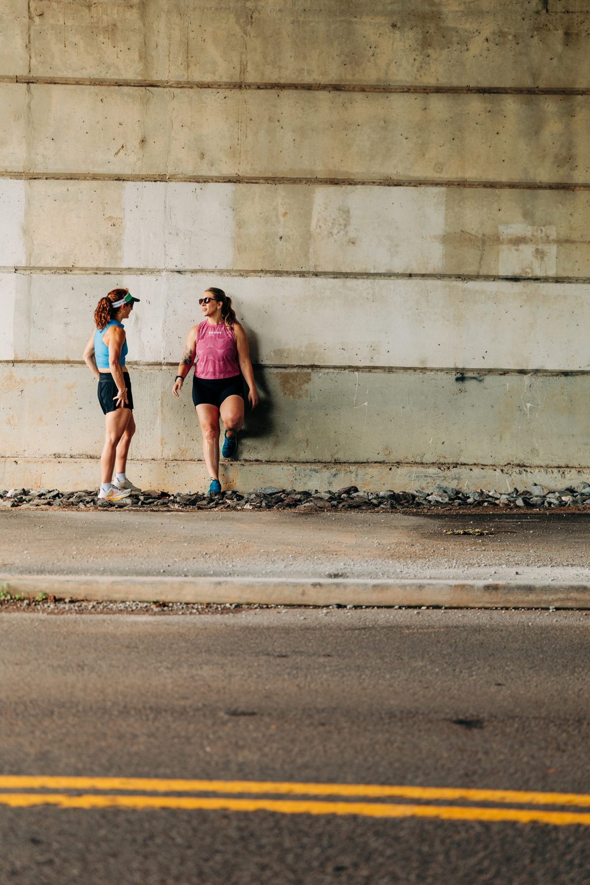 Two runners in BOUND gear talking against a concrete underpass wall